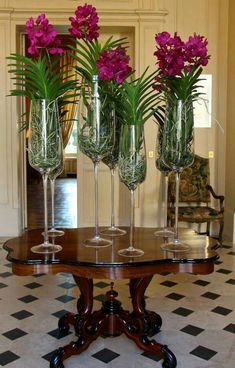 three wine glasses with purple flowers in them on a wooden table next to a black and white checkered floor