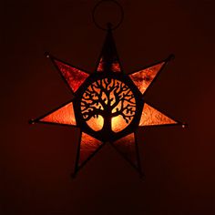 a stained glass star with a tree in the center on a dark background, lit by a candle light