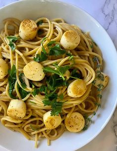 pasta with scallops and parsley in a white bowl on a marble table