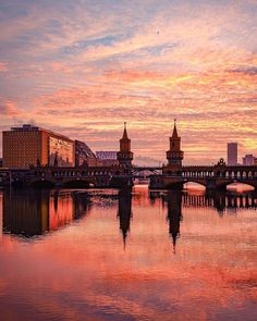 the sky is pink and orange as the sun sets over a river with buildings in the background