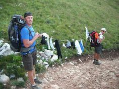 two men with backpacks are standing on the side of a hill