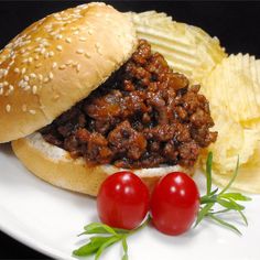 a sandwich with meat and potato chips on a white plate next to two cherry tomatoes