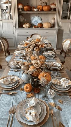 a dining room table set with plates and silverware, pumpkins in the background