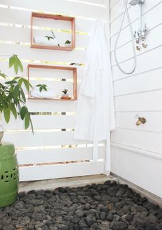 a bathroom with rocks on the floor and a green vase next to it in front of a shower