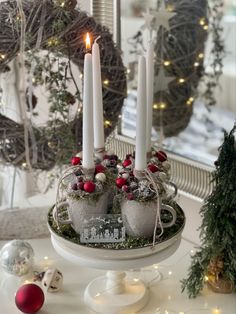 some white candles are sitting on a table with christmas decorations and wreaths in the background