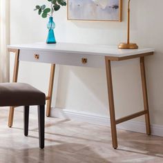 a white desk with a blue vase sitting on top of it next to a chair