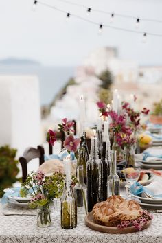 the table is set with flowers and candles on it, plates and bottles filled with food