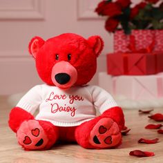 a red teddy bear sitting on top of a wooden floor next to a bouquet of flowers