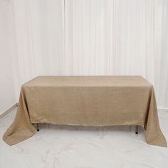 a table covered with a tan cloth in front of a white curtained wall and floor