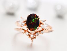 a black opal surrounded by white diamonds sits on top of a pink gold ring