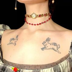 a woman with tattoos on her chest wearing a red beaded choker and earrings