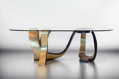 a glass table with metal legs and a curved design on the top, against a white background