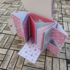 an open pink and white box on the ground with papers inside it, sitting on top of a wooden floor