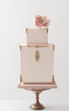 a pink and gold wedding cake sitting on top of a metal stand with a flower