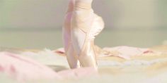 a ballerina's leg and ballet shoes on a bed with pink sheets in the background