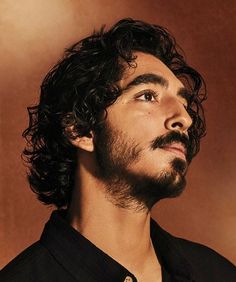 a man with curly hair and beard wearing a black shirt looking up to the sky