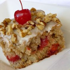 a piece of cake on a white plate with a cherry and walnut topping, topped with icing