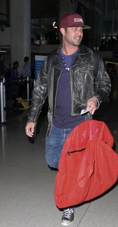 a man with a red bag is walking through the airport carrying his luggage and smiling