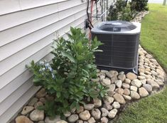 an air conditioner sitting on top of a pile of rocks next to a house