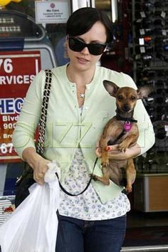 a woman holding a small dog in her arms while walking down the street with shopping bags