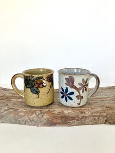 two coffee mugs sitting side by side on a wooden table next to each other