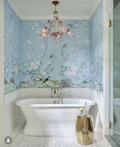 a white bath tub sitting under a chandelier next to a wall covered in flowers