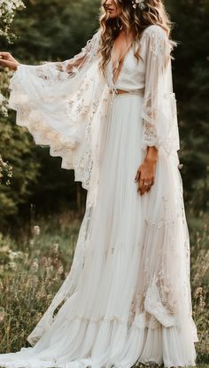 a woman wearing a white dress standing in the woods with her arms outstretched and hands out