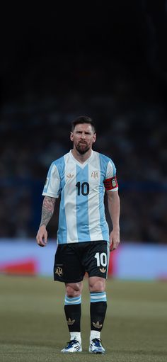 a man standing on top of a soccer field wearing a blue and white uniform with his hands in his pockets