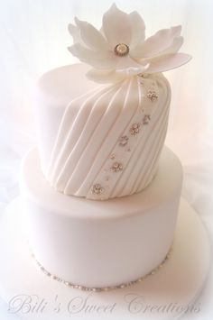 a white wedding cake with a large flower on the top and beaded ribbon around it