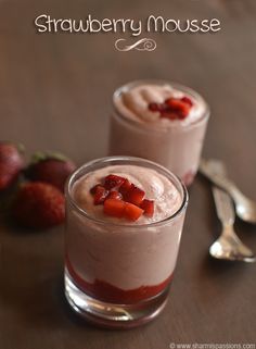 two desserts with strawberries and cream in them on a table next to spoons