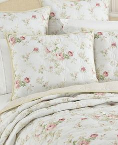 a white bed with pink flowers on it and a beige headboard in the background