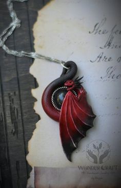 a red and black dragon pendant on a white piece of paper with writing in the background