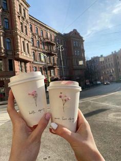 two people holding up coffee cups in the street