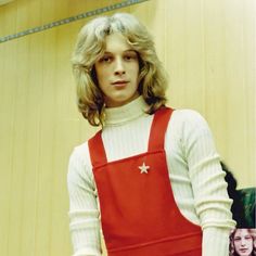 a man with long blonde hair wearing red overalls