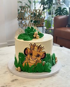 a birthday cake with a lion design on the top and green leaves around it, sitting on a table