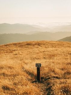 there is a sign on the top of a hill with mountains in the back ground