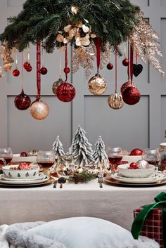 a christmas table setting with ornaments hanging from the ceiling and plates on top of it