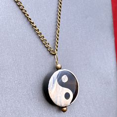 a black and white necklace with a yin symbol on it's center piece, hanging from a gold chain