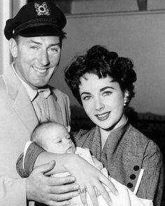 a man in uniform holding a baby and smiling at the camera while standing next to a woman