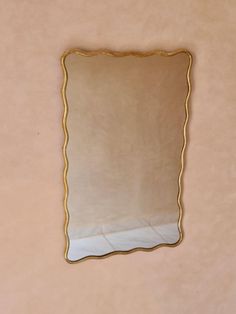 a mirror hanging on the wall with a gold trim around it's edge and an empty shelf below