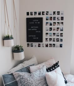 a bed with many pillows and pictures on the wall above it, along with hanging planters