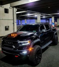 a black truck is parked in a parking garage with its lights on and it's hood up