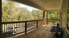 a wooden porch with two chairs and a table on the front deck overlooking a wooded area