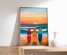 three surfboards on the beach at sunset with water in the background, framed print