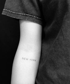 a black and white photo of a person with a new york tattoo on their arm