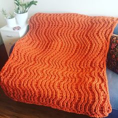 an orange knitted blanket sitting on top of a blue couch next to a potted plant