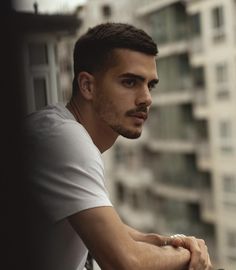 a man with a goatee and white shirt leaning on a railing looking off into the distance