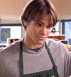 the young man is wearing an apron and looking down at something in front of him