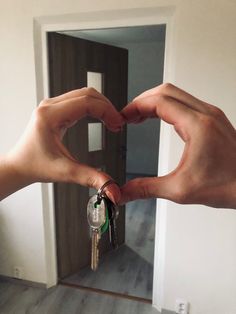 two hands making a heart shape with their fingers holding keys in front of an open door