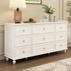 a white dresser sitting in a living room next to a lamp and painting on the wall